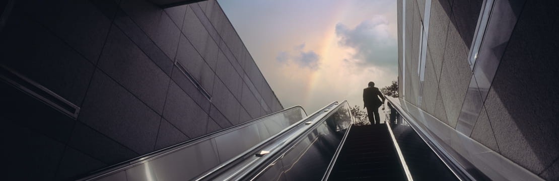 Person ascending an escalator toward daylight, symbolizing 2026 tax law changes limiting high earners’ pre-tax catch-up retirement contributions.